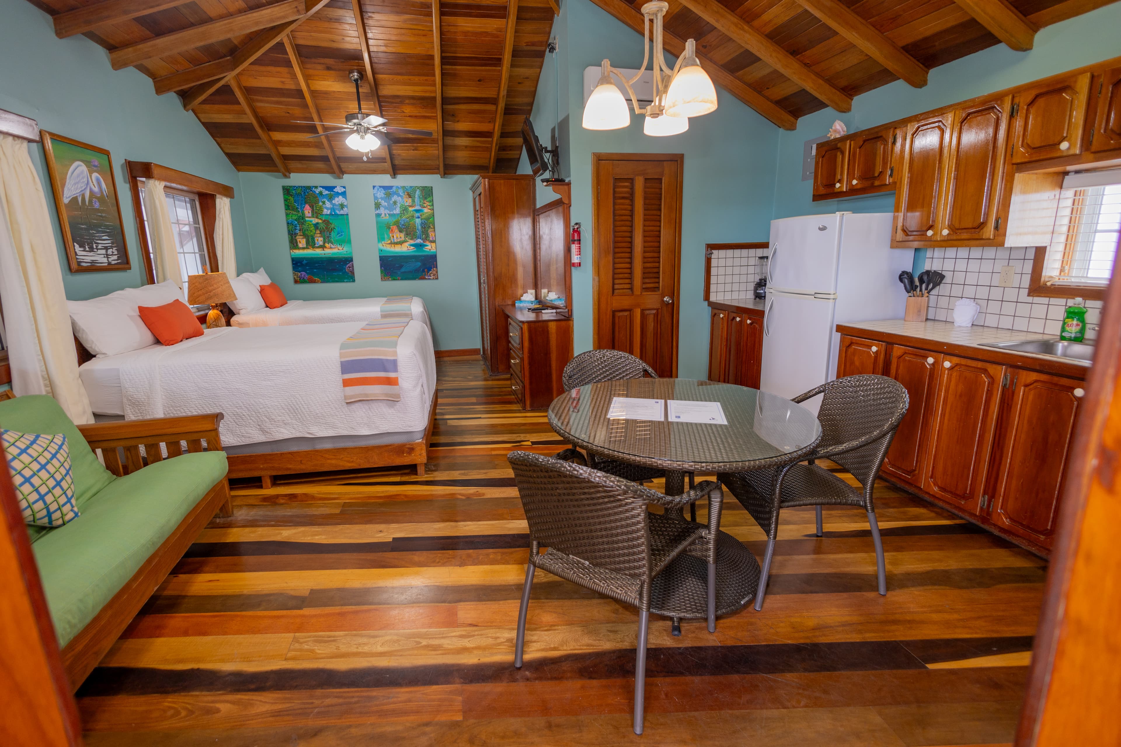 A cozy cabin interior featuring two beds, a dining table, and a kitchenette with wooden accents.